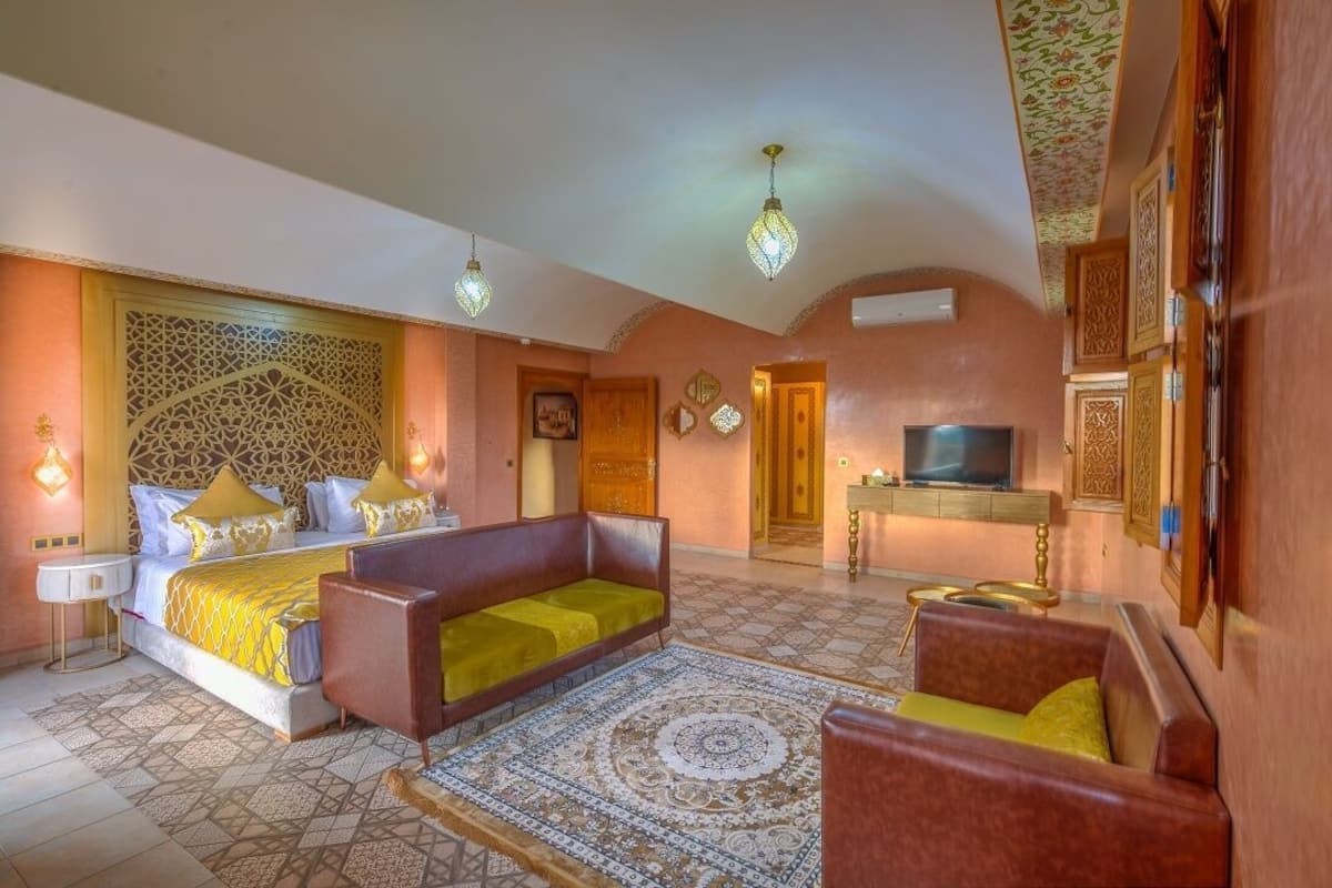 A hotel room with a bed, two sofas, a TV, and a decorative ceiling.