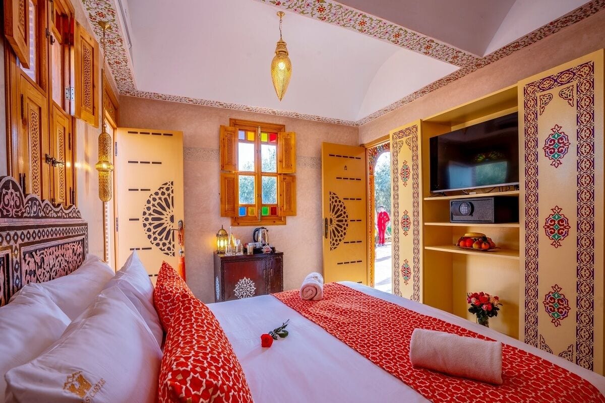 A hotel room with two beds, a television, a minibar, and decorative wall patterns.