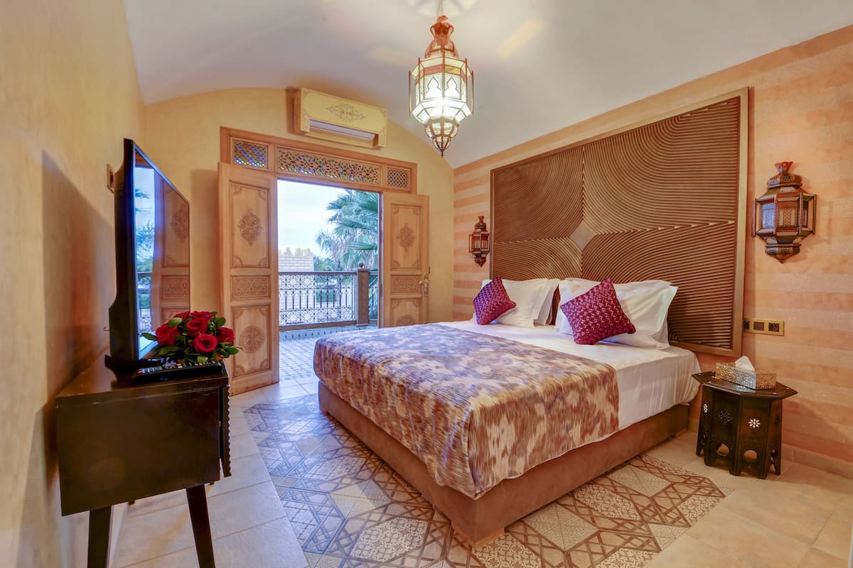 A bedroom with a large bed, a TV on a stand, and a decorative wall panel.