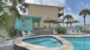 A pool area with a hot tub, lounge chairs, and a building with a balcony.