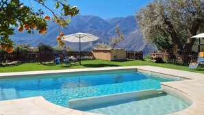 A swimming pool with a view of mountains, a fenced garden, and a lounge area with an umbrella. - Villa Tropical; High Standard Space Calm, Eco-Property Saltwater-Pool Child-Safe (Cortijo el Potro)