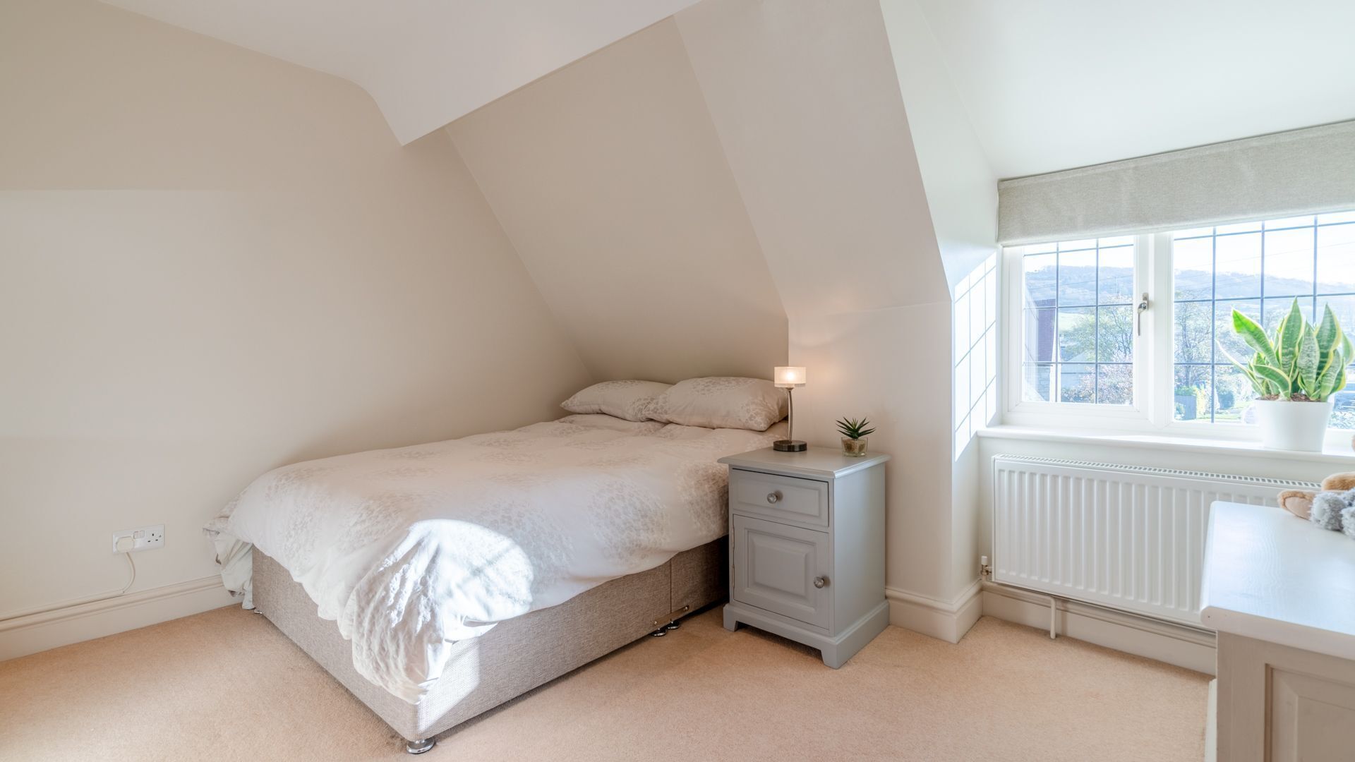 A bedroom with a bed, bedside table, lamp, and a window with a view.