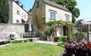 A stone building with a garden, outdoor seating, and a wooden pergola.