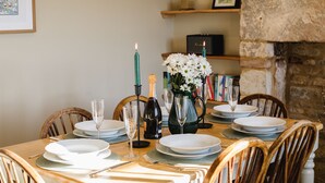A dining table set with plates, glasses, a bottle of champagne, and a vase of flowers. - Rose Cottage, Rodborough - sleeps 6 guests  in 3 bedrooms (Stroud)