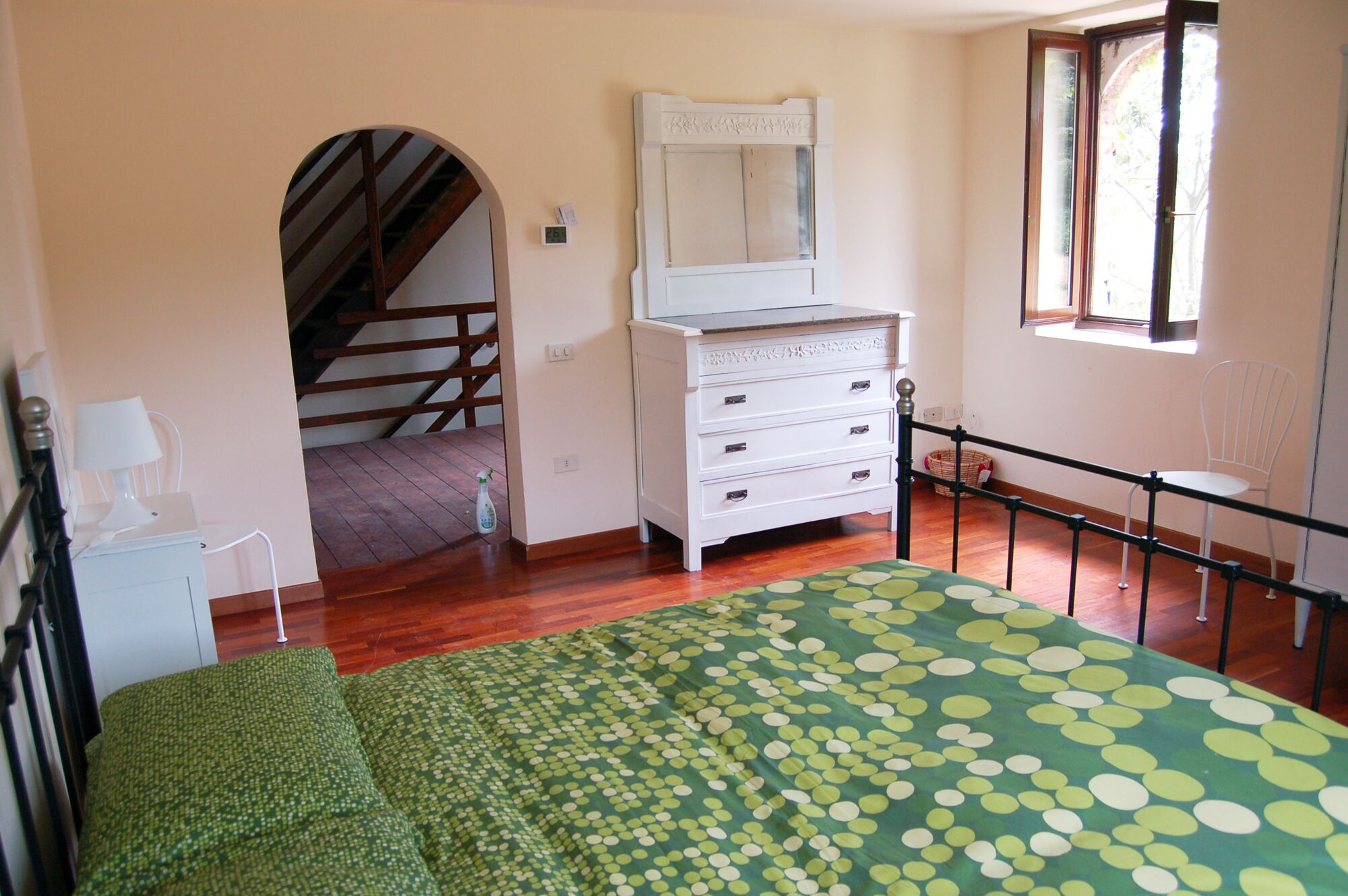 A bedroom with a bed, dresser, mirror, and a window.