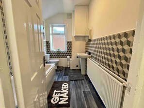 A narrow bathroom with a toilet, sink, and a radiator.