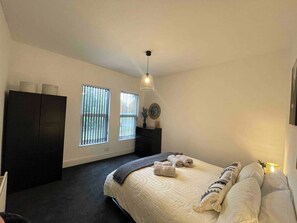 A bedroom with a bed, a wardrobe, a desk, and two windows.