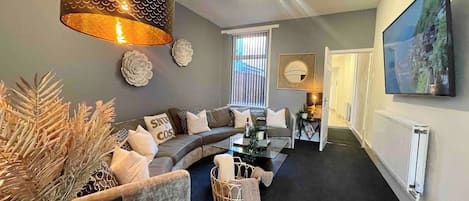 A modern living room with a sectional sofa, a coffee table, and a large TV mounted on the wall.