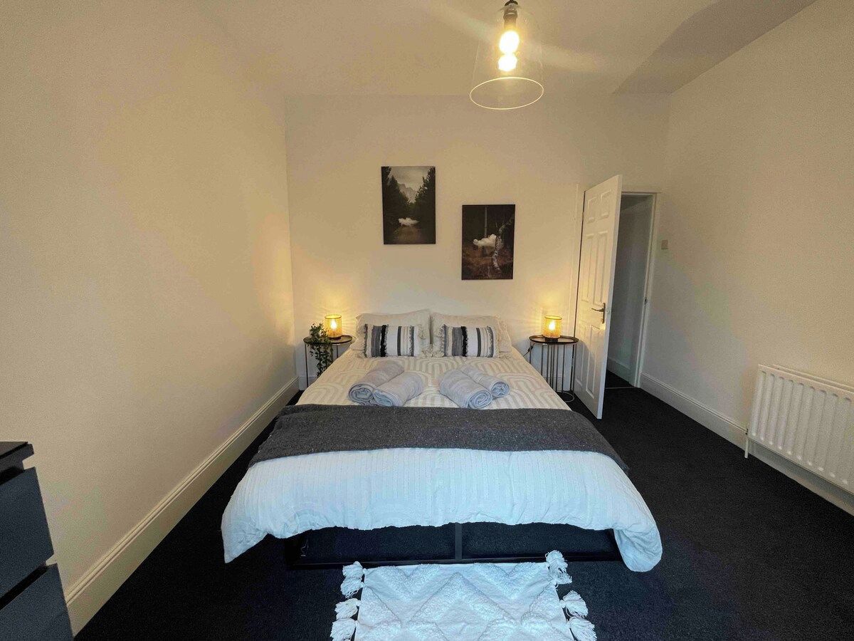 Ein Schlafzimmer mit einem Bett, Nachttischen, einem Heizkörper und zwei gerahmten Bildern an der Wand.