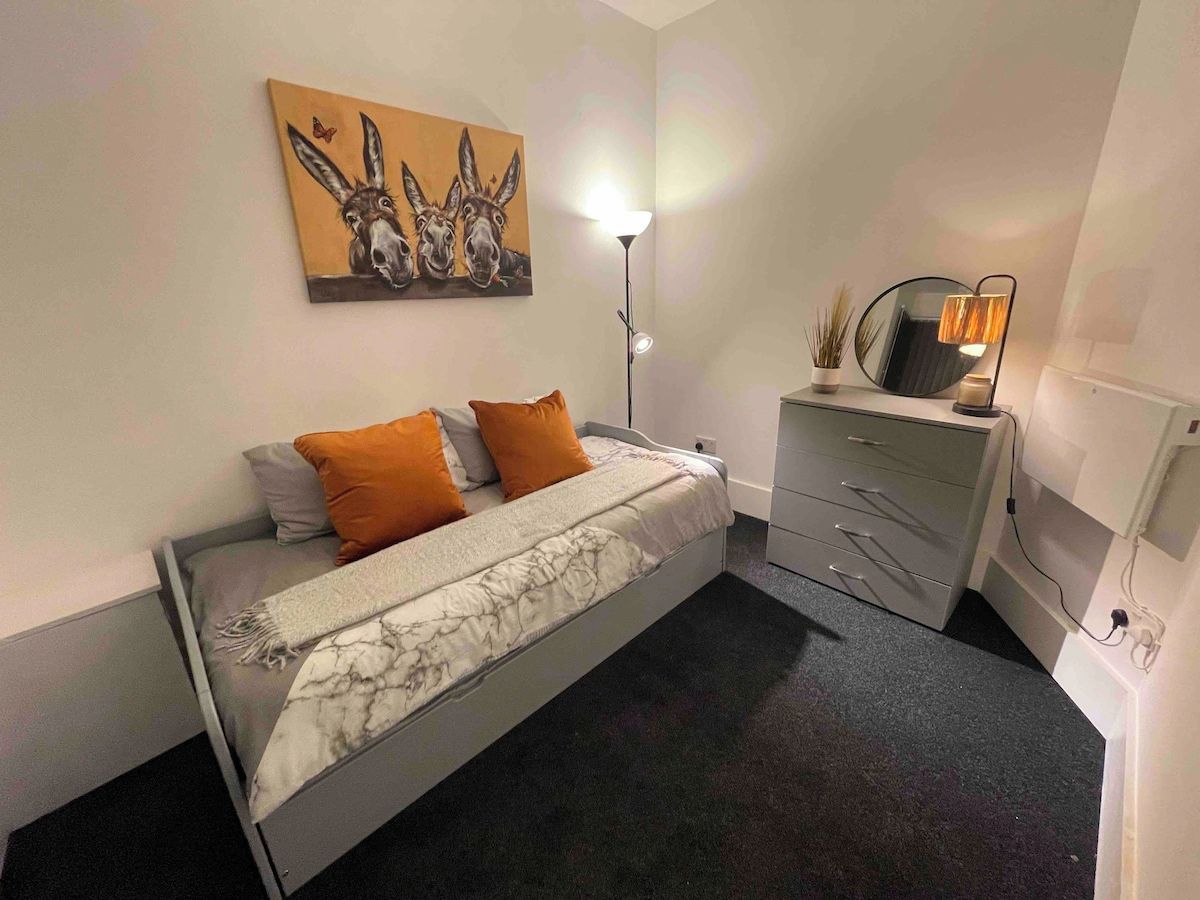 Ein Schlafzimmer mit einem Bett, einem Nachttisch, einer Lampe, einem Spiegel und einem Wandbild.