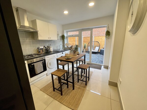 A modern kitchen with white cabinets, a gas stove, and a dining area with a wooden table and stools. - Urban 3 Bedroom Home in Kings Heath-Great Location (King's Heath)