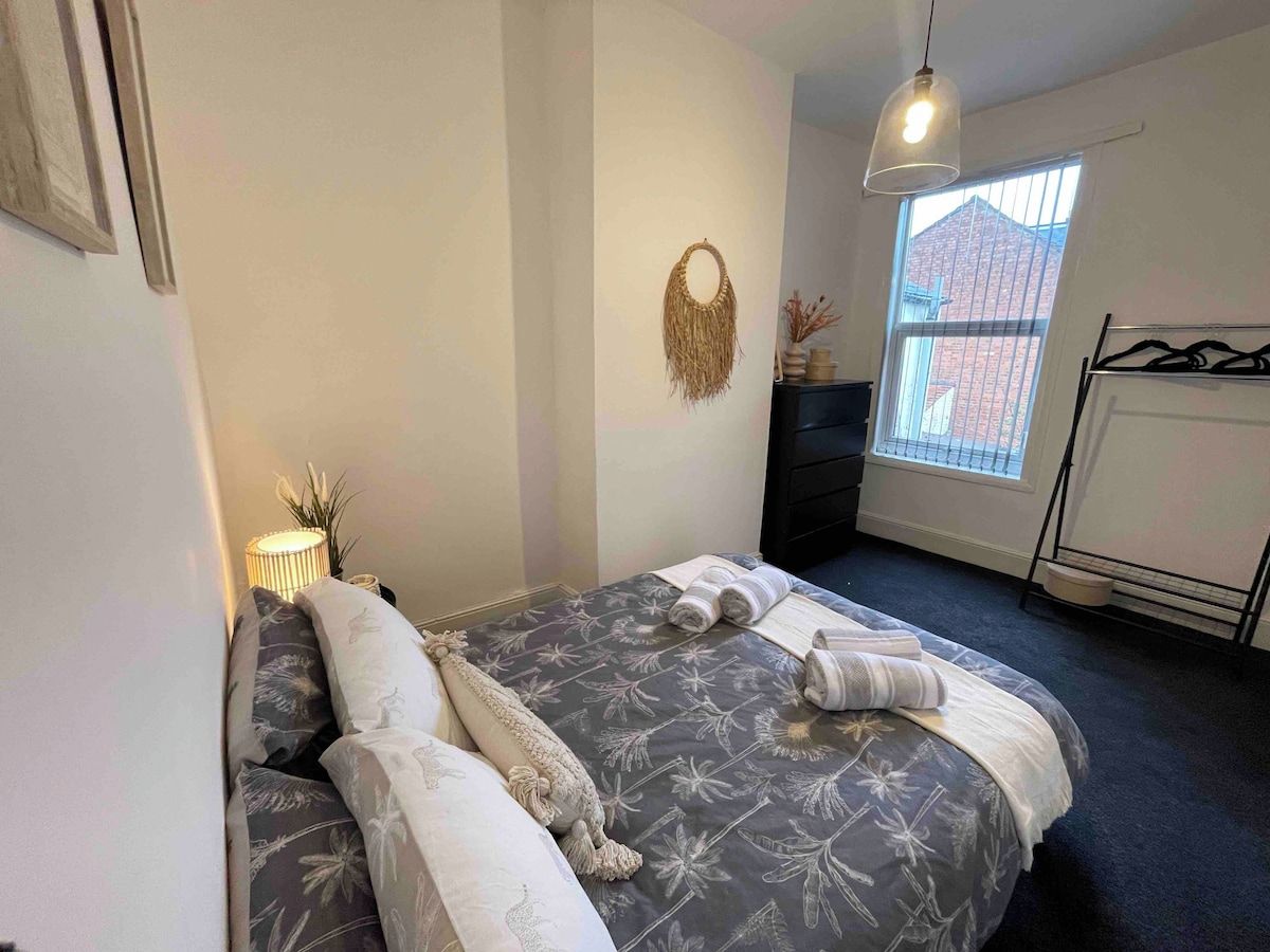 A bedroom with a bed, a hanging light fixture, a window, and a radiator.