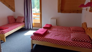 Une chambre avec deux lits, chacun agrémenté de draps rouges et de motifs en forme de cœur. Une fenêtre offre une vue sur la verdure environnante.
