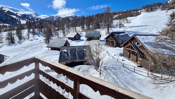 Un village de montagne enneigé, avec des chalets en bois et un ciel d’un bleu limpide.