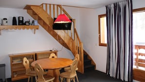 Un coin repas avec une table et des chaises en bois, un escalier avec une rampe en bois, un luminaire suspendu rouge et une fenêtre avec des rideaux à rayures.