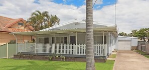 A single-story house with a covered porch, a fenced yard, and a palm tree.