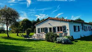 A two-story house with a tiled roof, a covered patio with outdoor furniture, and a well-maintained lawn. - Le Grand Cottage Nature Piscine Chauffée Privée (Peyrole)
