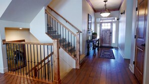 A wooden staircase with a glass railing, a hallway with a wooden floor, a door with a window, and a hanging light fixture. - Luxurious Mountain Home with 7 BRs private hot tub (Eden)