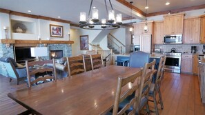 A spacious living room with a fireplace, a dining area with a wooden table and chairs, a kitchen with wooden cabinets, and a staircase leading to another level. - Luxurious Mountain Home with 7 BRs private hot tub (Eden)