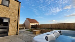 Een achtertuin met een jacuzzi, een bakstenen huis, een houten terras en een houten omheining.