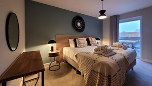 Een hotelkamer met een bed, nachtkastje, spiegel, een wandlamp en uitzicht op het buitengebied.