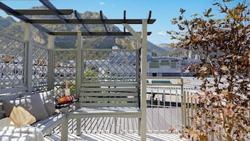 A covered outdoor seating area with a bench, a table, and a bottle of champagne.