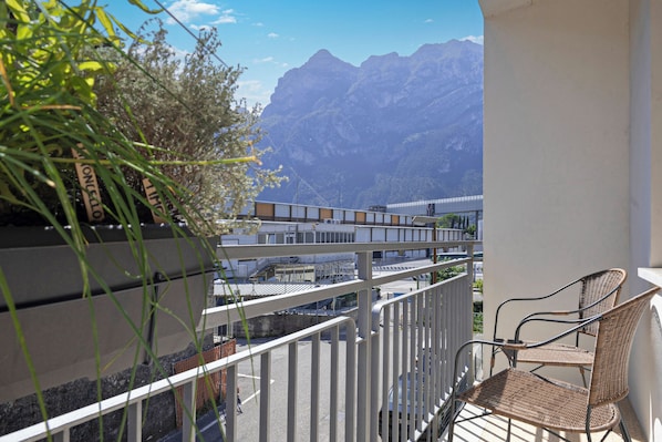 A balcony with a wicker chair, a white railing, and a mountain view.