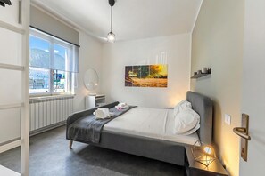 A modern hotel room with a bed, bedside table, window, radiator, and a painting on the wall.