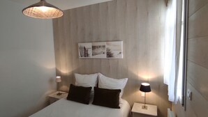 Un dormitorio moderno con cabecera de madera, cama con ropa de cama blanca, dos mesitas de noche con lámparas y una obra de arte colgada en la pared.