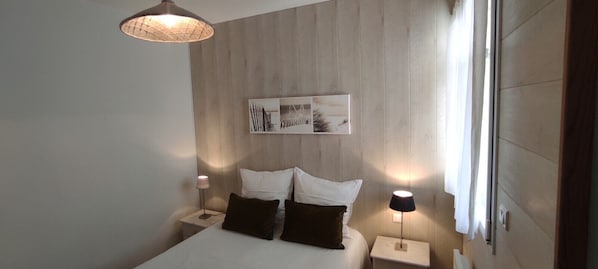 A modern bedroom with a wooden headboard, a bed with white linens, two bedside tables with lamps, and a wall-mounted artwork.