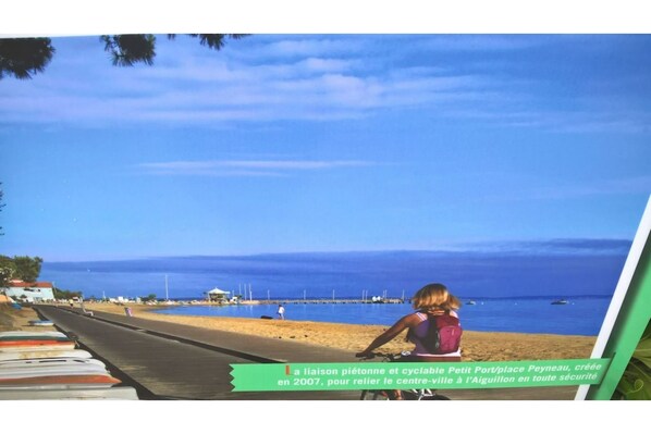 A beach scene with a clear sky, a person on a bicycle, and a signboard.