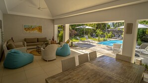 Un salon moderne avec vue sur la piscine, des meubles en osier et un coin repas.