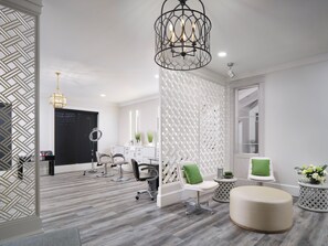 Experience a serene atmosphere in our stylish salon, featuring a spacious reception area with a round mirror, comfortable seating, and a decorative chandelier.