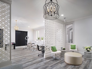 Experience a serene atmosphere in our stylish salon, featuring a spacious reception area with a round mirror, comfortable seating, and a decorative chandelier.