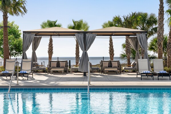 A poolside area with lounge chairs, a covered seating area, and a clear view of the ocean.