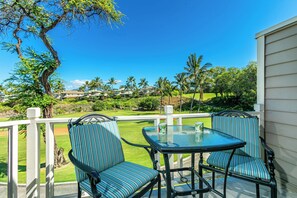 A patio with two chairs and a table, overlooking a golf course and residential buildings.