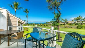 An outdoor patio with a glass table and chairs, a white railing, and a view of a golf course and ocean. - Grand Champions #86 Gorgeous Views On Golf Course, Near Popular Beaches (Wailea)