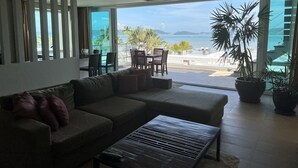 Un salon moderne avec un canapé, une table basse et un coin repas. Une grande fenêtre offre une vue sur la plage et l’océan.