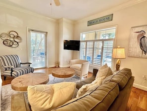 Una sala de estar con un sofá, sillones, una mesa de centro, un televisor y un letrero que dice 'BEACH HOUSE'.
