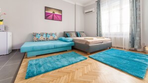 A modern bedroom with a sofa, a bed, and two blue rugs on a wooden floor. - Real Apartments Wesselényi III.  (Budapest)