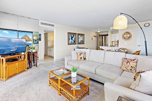 A living room with a television, sofa, coffee table, and a dining area with chairs.