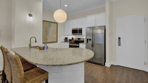 A kitchen with white cabinets, a granite countertop, stainless steel appliances, and wicker chairs. - Pet Friendly, Updated 1 Bedroom Getaway at Ocean Suites (Saint Simons Island)