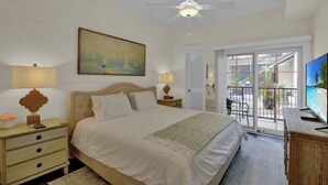 A bedroom with a bed, nightstands, a painting, a ceiling fan, and a view of the outside balcony. - Pet Friendly, Updated 1 Bedroom Getaway at Ocean Suites (Saint Simons Island)