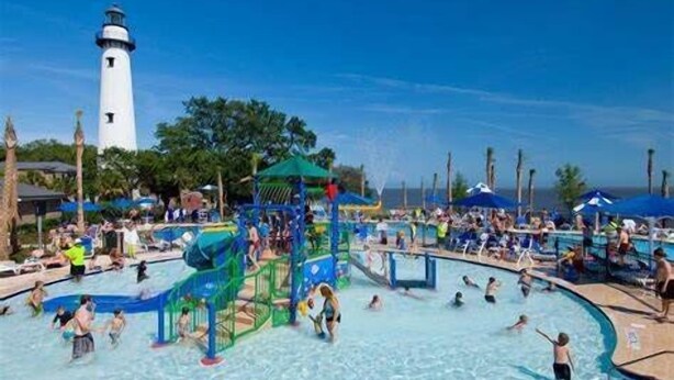 A water park with multiple pools, a lighthouse in the background, and people enjoying the facilities. - Pet Friendly, Updated 1 Bedroom Getaway at Ocean Suites (Saint Simons Island)