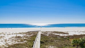 Une plage avec une promenade en bois qui mène à l’océan, des dunes de sable et un ciel bleu clair.