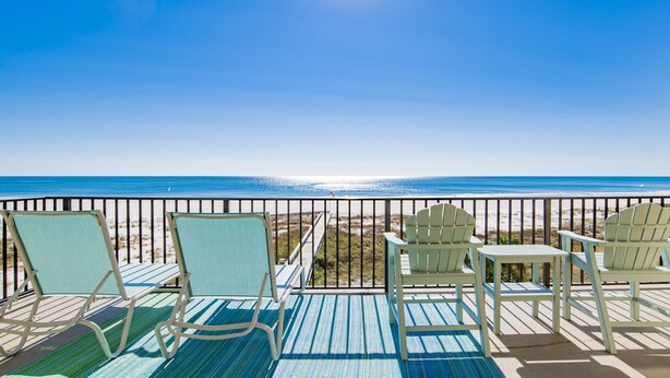 Une terrasse avec quatre chaises Adirondack et une petite table, offrant une vue dégagée sur la plage et l’océan.