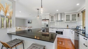 Una cocina moderna con armarios blancos, electrodomésticos de acero inoxidable y una isla central con taburetes de bar.