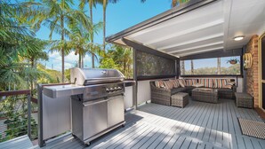 Eine Außenpatio mit integriertem Grill, Korbmöbeln und Blick auf Palmen.