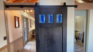 Ein Flur mit einer dunklen Tür, drei blauen Fenstern, Holzboden und einer Treppe mit Holzgeländer.