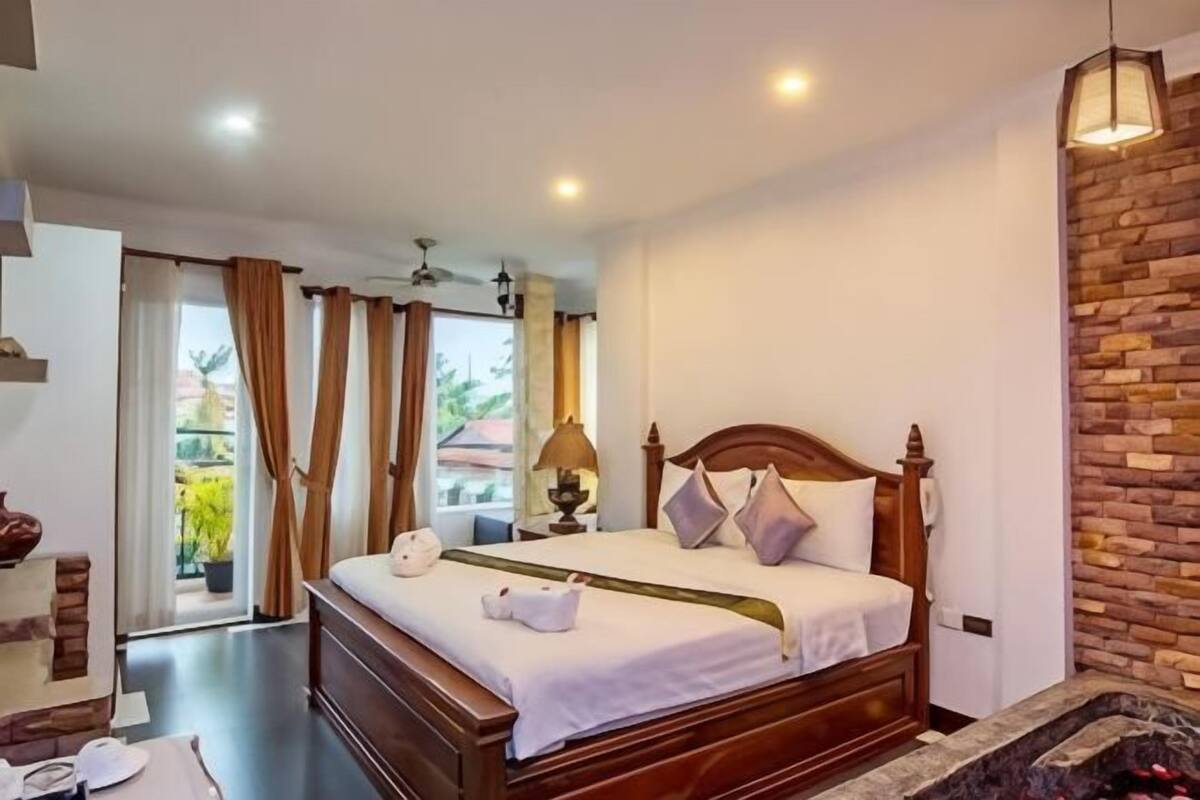 A bedroom with a wooden bed, a brick accent wall, and a view of the outdoors.